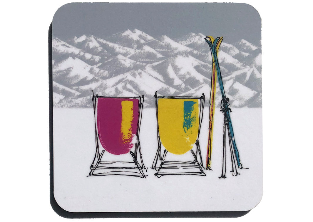 Art coaster of 2 pink and mustard deckchairs in the snow with skis, poles, grey sky and mountain backdrop by artist Hannah van Bergen