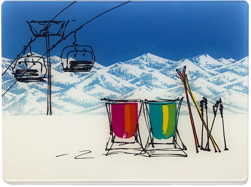 Glass platter / worktop saver with artwork of 2 deckchairs in the snow with mountain backdrop, skis and chair lift by artist Hannah van Bergen