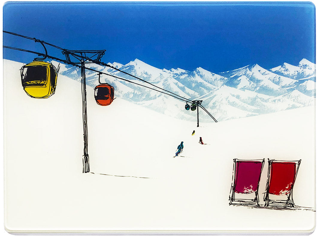 Glass platter / worktop saver with artwork of 2 deckchairs in the snow with mountain backdrop, skiers and bubble lift by artist Hannah van Bergen