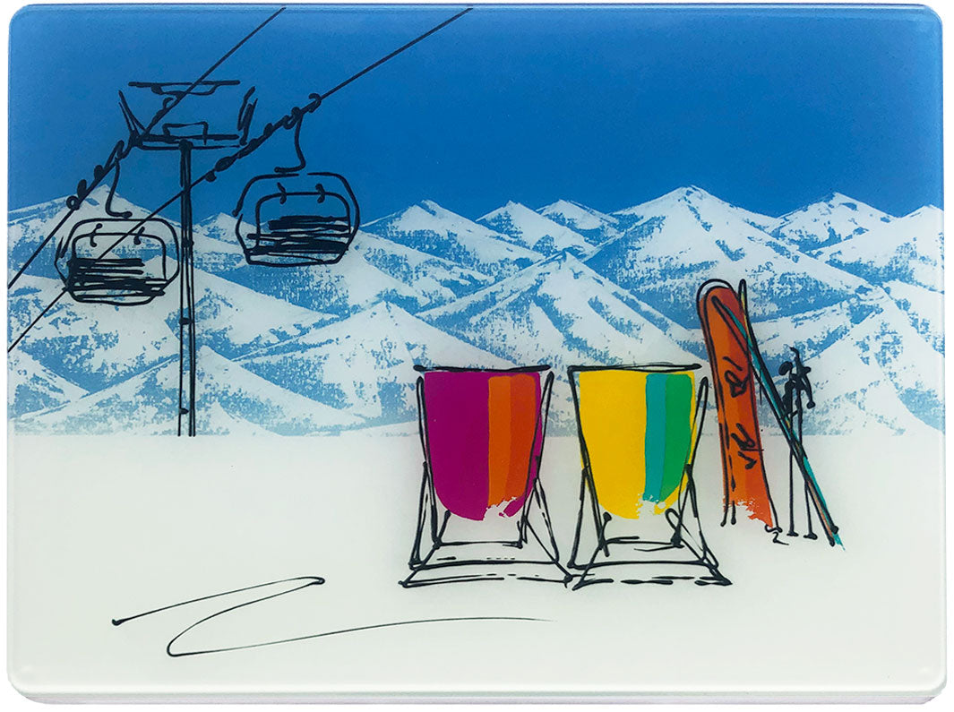 Glass platter / worktop saver with artwork of 2 deckchairs in the snow with mountain backdrop, one snowboard and one set of skis and chair lift by artist Hannah van Bergen
