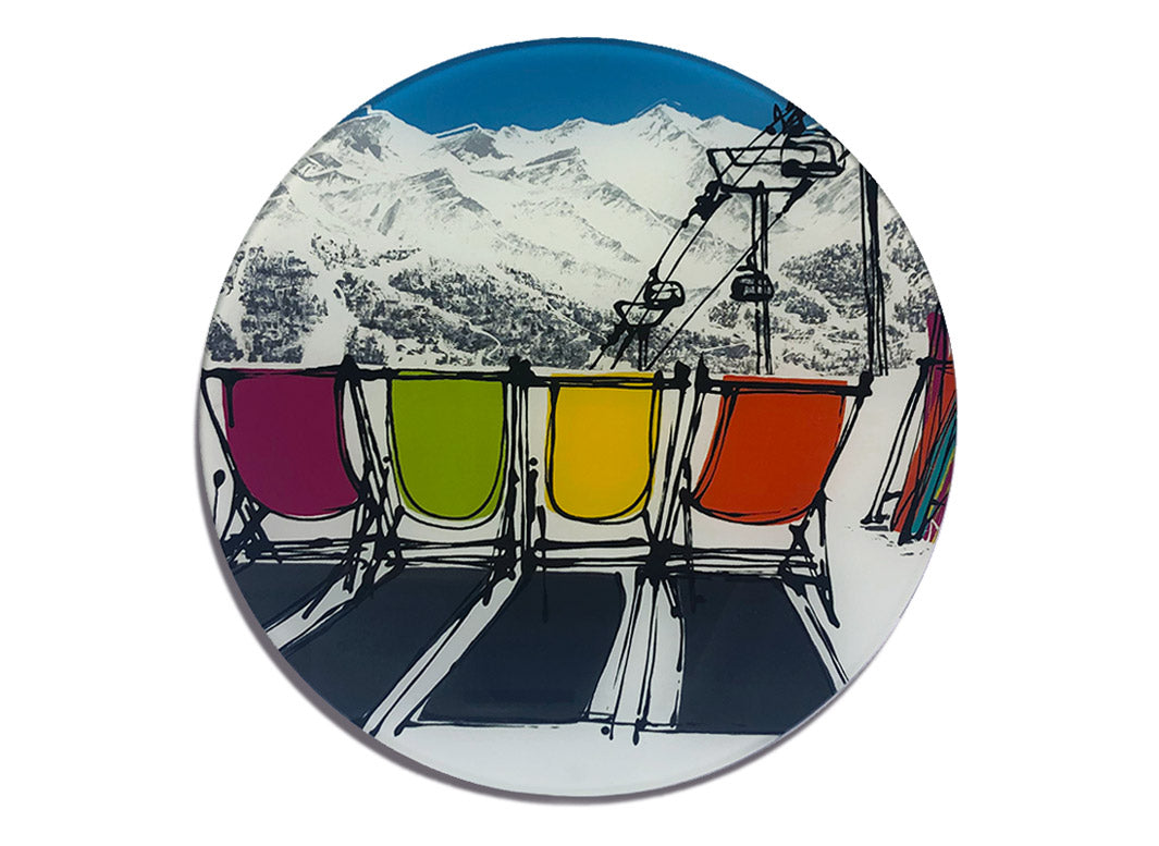 Round glass platter / worktop saver with artwork of four deckchairs in the snow with mountains backdrop, skis and chair lift by artist Hannah van Bergen